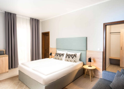 Ein Doppelzimmer mit Kommode, Bett, Lampen und Vorhängen im Arthotel ANA Eden