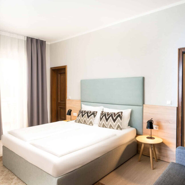 Ein Doppelzimmer mit Kommode, Bett, Lampen und Vorhängen im Arthotel ANA Eden