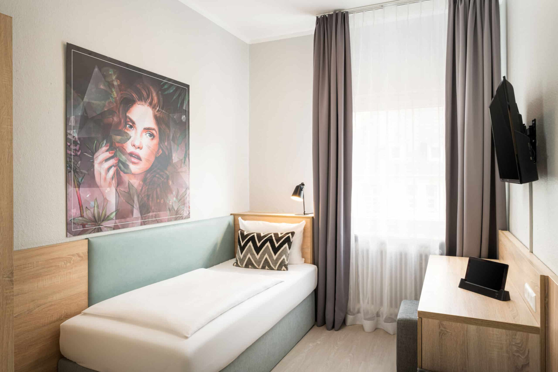 Ein Einzelzimmer mit Bett, Schreibtisch, Fernseher und Vorhängen im Arthotel ANA Eden