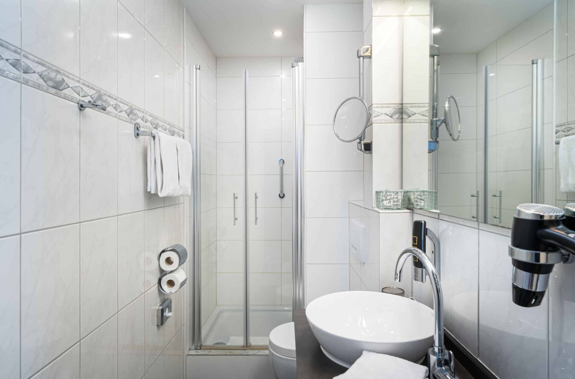 Ein Badezimmer mit Föhn, Spiegeln, Toilette und Dusche im Arthotel ANA Liberty Bremen