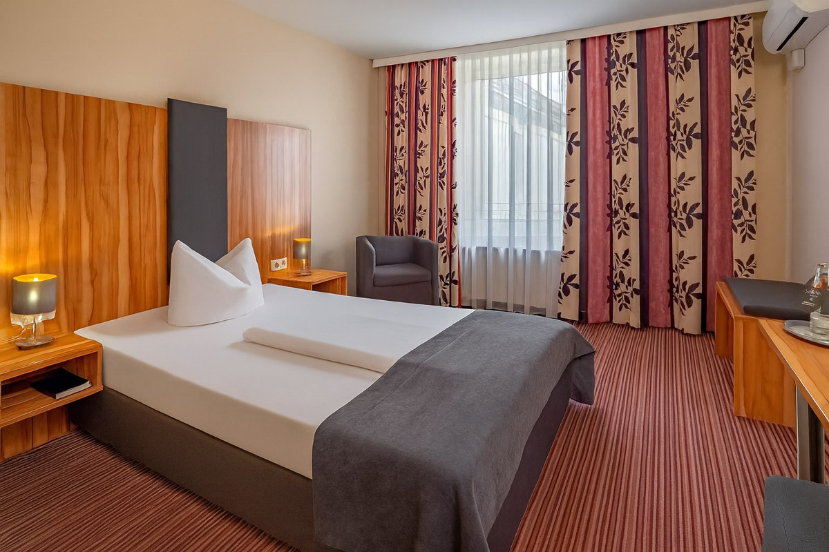 Ein Einzelzimmer mit Schreibtisch, Sessel und Nachttischen im Arthotel ANA Style