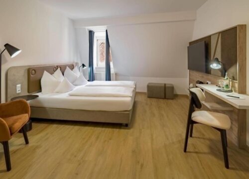 Ein Doppelzimmer mit Fenster, Fernseher, Schreibtisch und Sessel im Aspire Kronprinz 