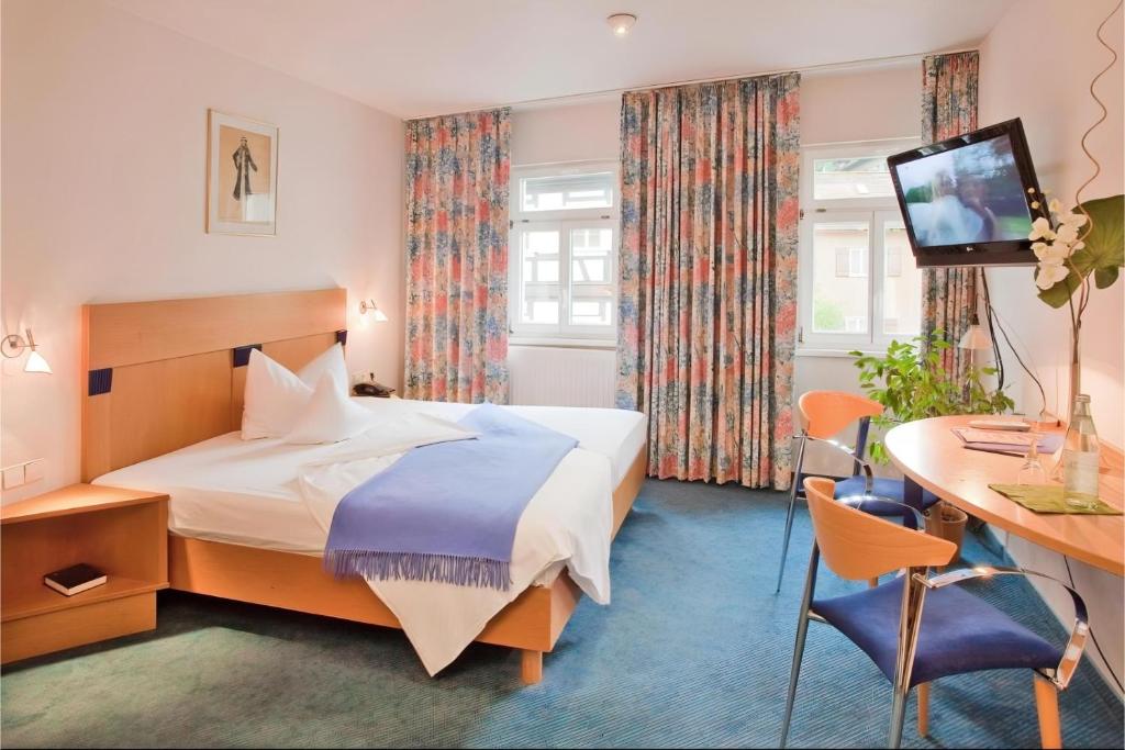 Ein Doppelzimmer mit Schreibtisch und zwei Fenstern im Aspire Kronprinz 