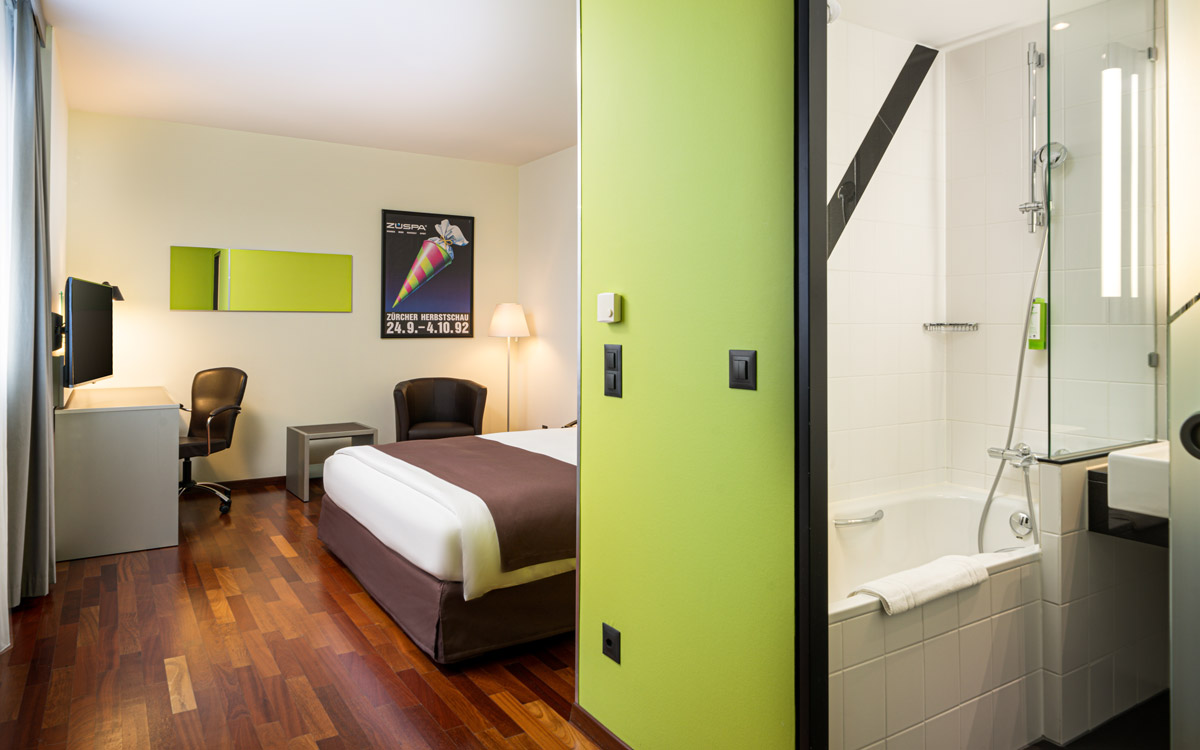 Das Badezimmer und der Schlafbereich eines Zimmers im Holiday Inn Zürich Messe