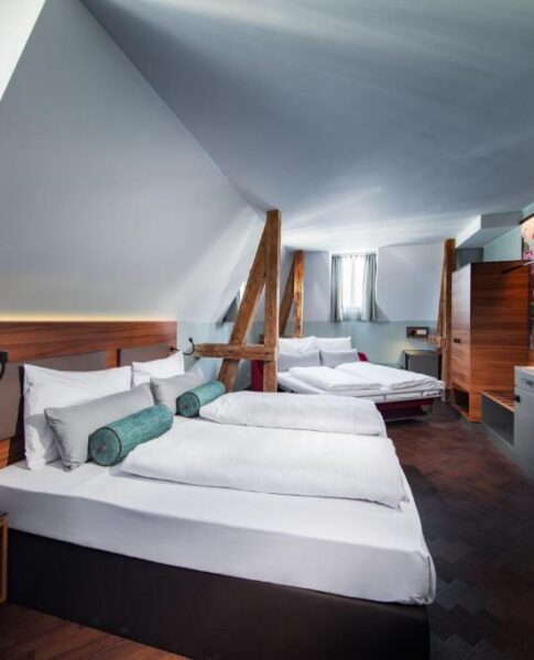 Die Betten und der Fernseher eines Vierbettzimmers im Maison Schiller