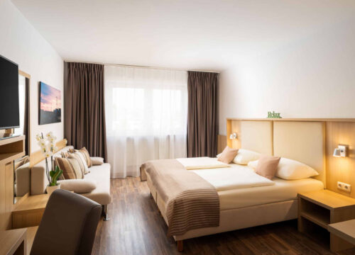 Das Doppelbett und das Sofa eines Standardzimmers im QU Hotel Augsburg