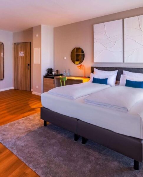 Das Doppelzimmer mit Doppelbett, Nachttischen und Kaffeemaschine im Ramada Encore by Wyndham Munich Messe